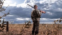 Человек в поле с вскинутым на плечо охотничьем ружьем.